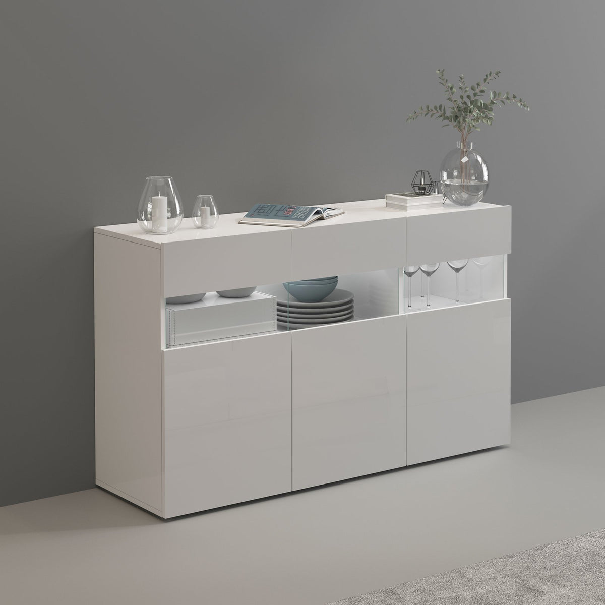 Credenza CREDENZA bianco opaco in ambiente grigio, con un'anta aperta che mostra piatti e calici