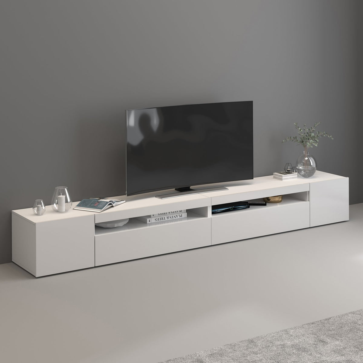 Porta TV bianco opaco in soggiorno con televisore, candele e libri nei vani