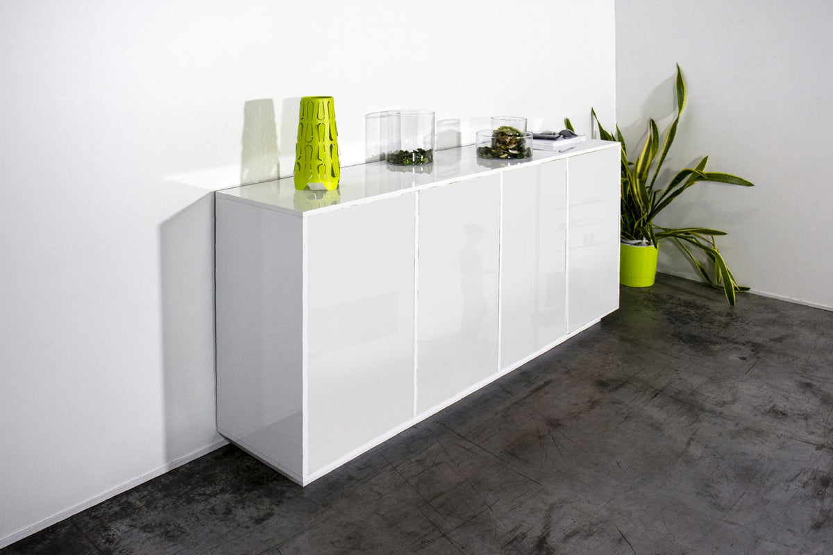 Credenza ENIGMA bianco lucido appoggiata a parete bianca, vista tre quarti con vasi decorativi #colore_Bianco Lucido