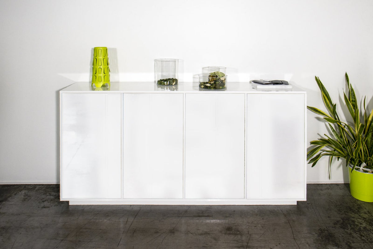 Credenza ENIGMA bianco lucido frontale con ante chiuse e vaso verde su pavimento grigio #colore_Bianco Lucido