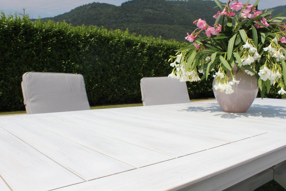 Tavolo da giardino LOMBOK bianco chiuso in giardino con vaso di fiori e sedie grigie