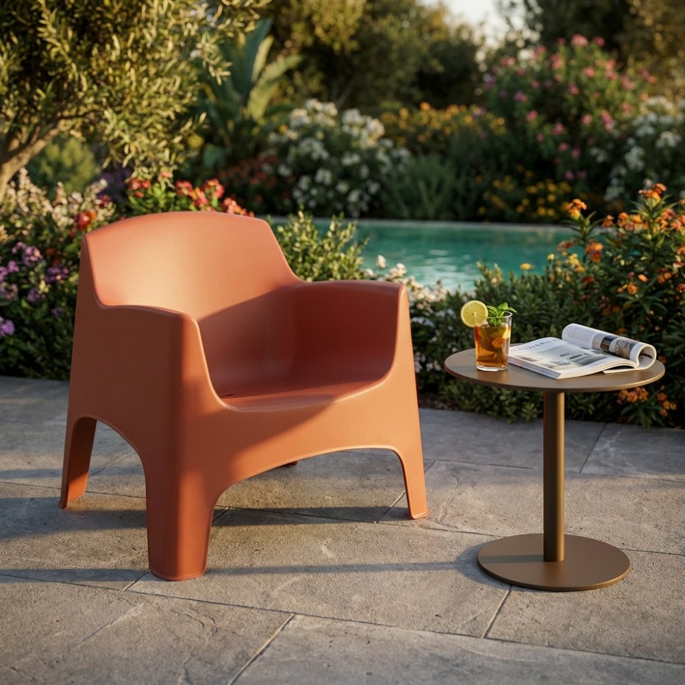 Poltrona IBIZA rosso terracotta di tre quarti su pietra con bicchiere e rivista sul tavolino bronzo