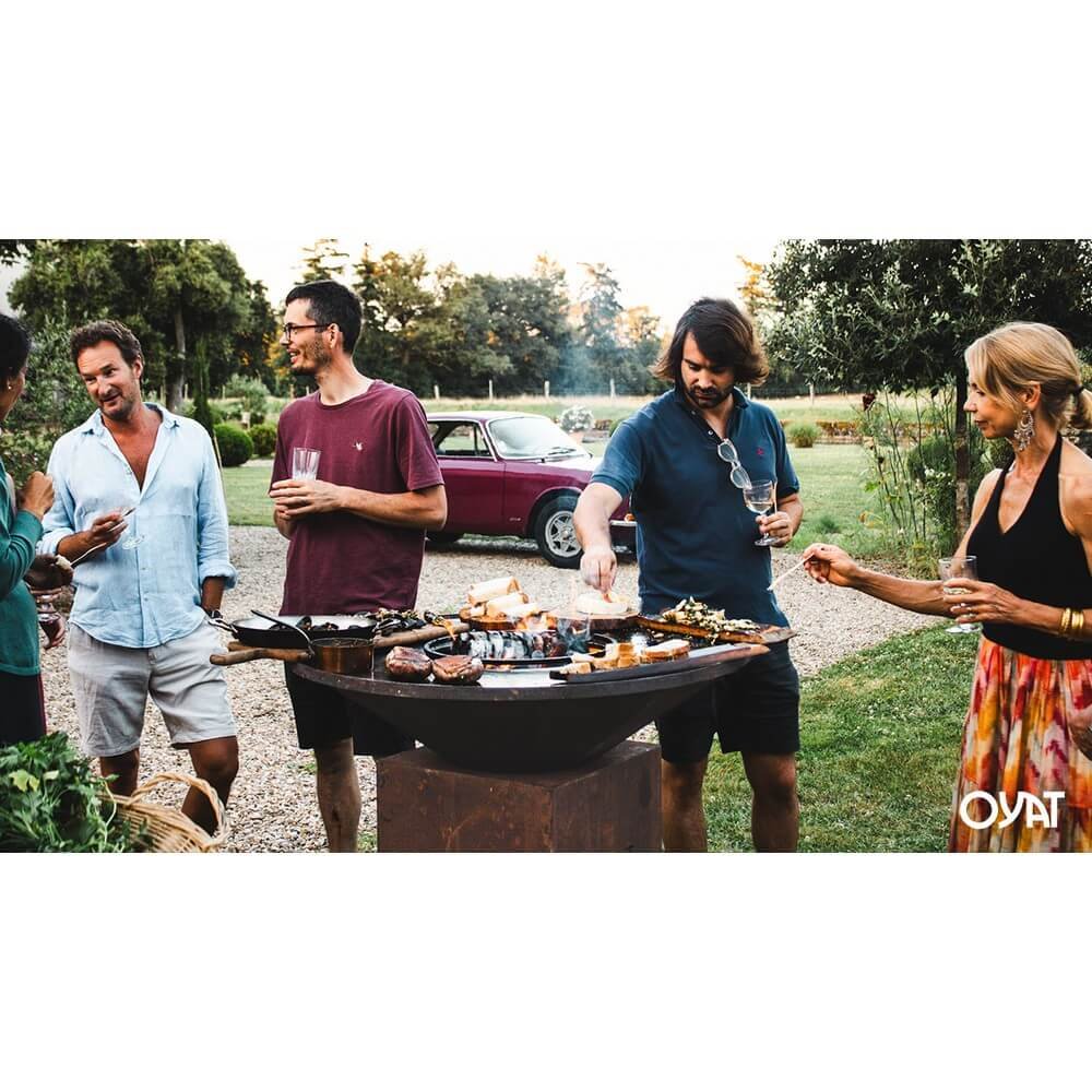 Barbecue OYA BBO 68 nero in giardino con cinque persone che cucinano attorno al braciere