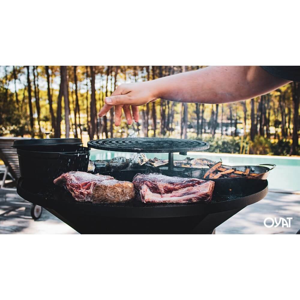 Barbecue OYA BBO 68 nero con griglia e carne cruda sul bordo, in giardino con piscina