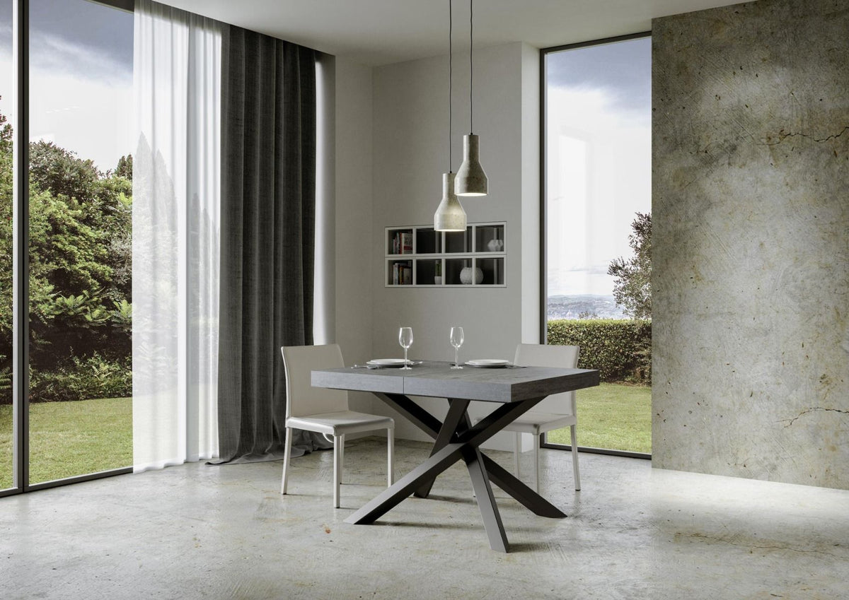Tavolo VOLANTIS cemento grigio scuro con base a X antracite, apparecchiato con due calici #colore_Cemento