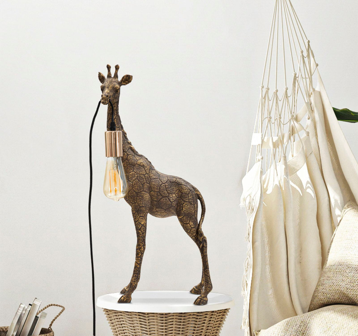 Lampada GIRAFFA oro accesa su piano bianco in un salotto con amaca e cesto di vimini #dimensione_28x60x16