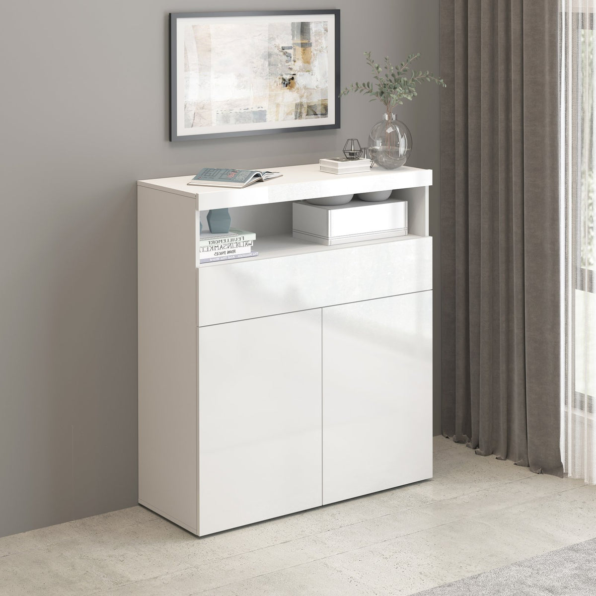 Credenza alta bianco opaco con due ante e cassetto, in soggiorno accanto a una tenda grigia