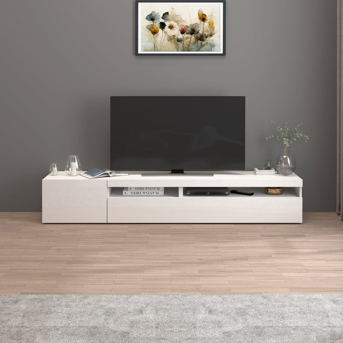 Porta TV bianco opaco visto frontalmente con vani a giorno e libri su pavimento in legno