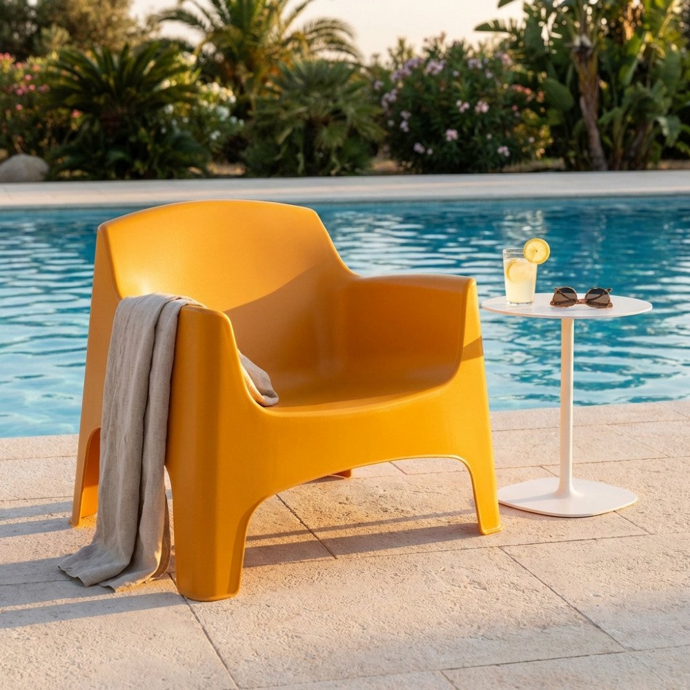 Poltrona monoblocco IBIZA giallo di tre quarti su pietra chiara, con tavolino bianco accanto