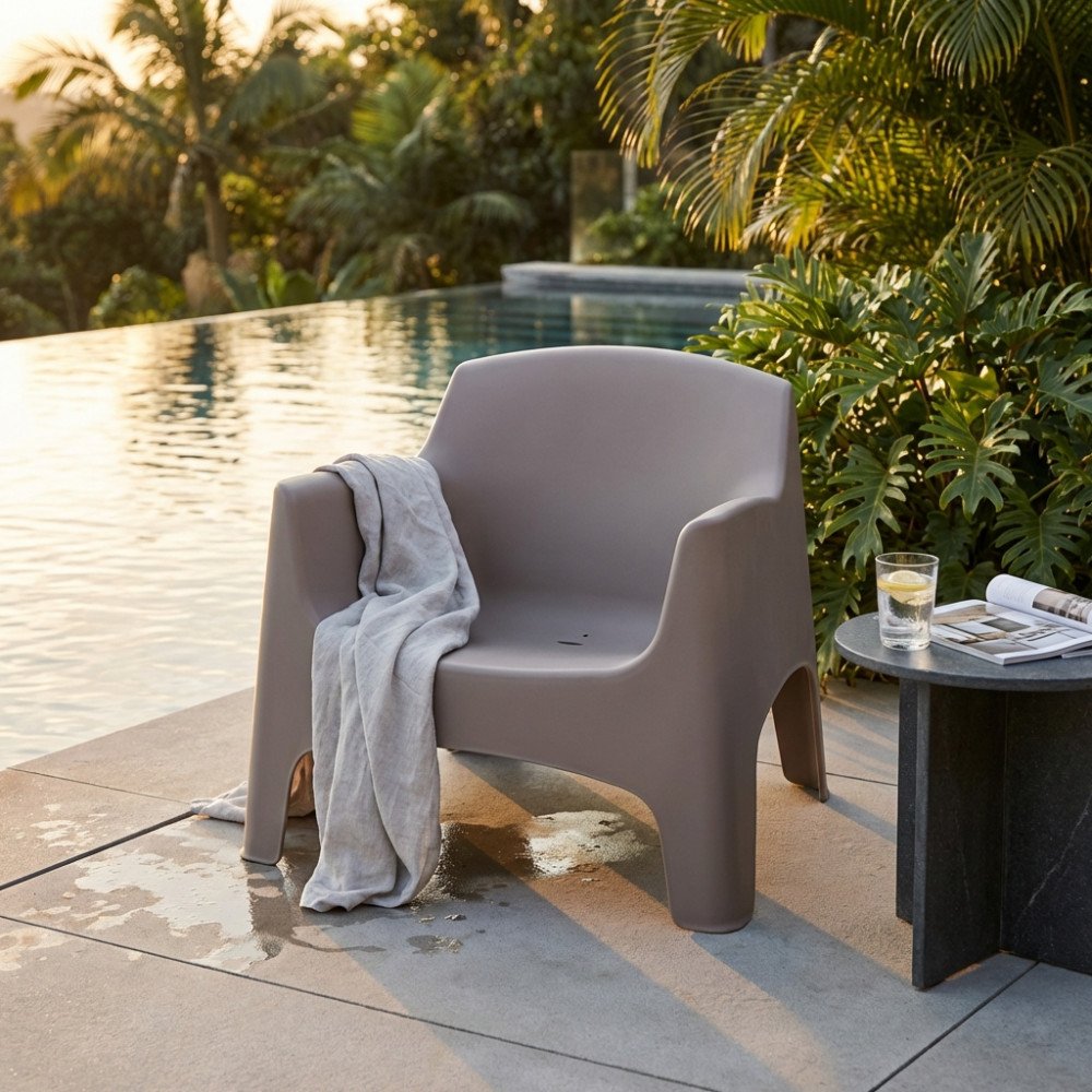 Poltrona IBIZA taupe in esterno accanto alla piscina, con palme e tavolino sullo sfondo