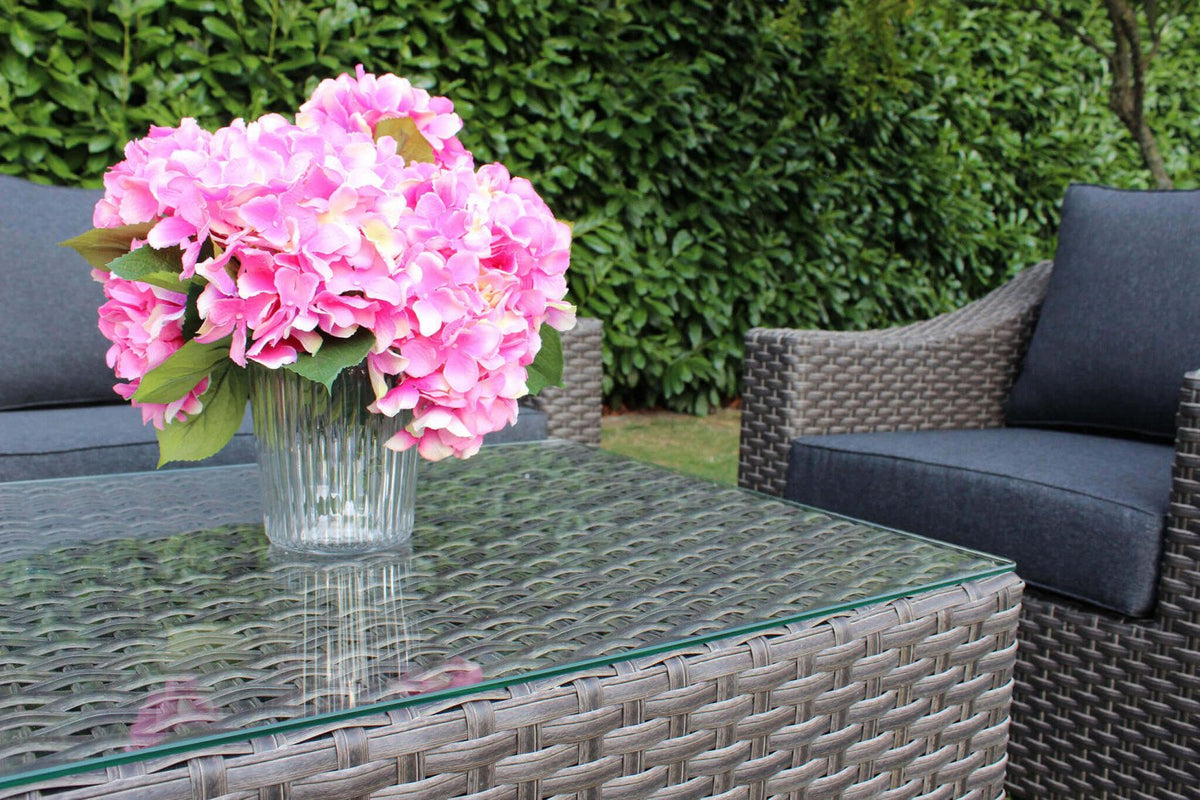 Tavolino da giardino LANZAROTE in rattan grigio con piano in vetro, vaso di ortensie sopra